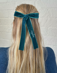 teal bow on blonde hair against a brick wall