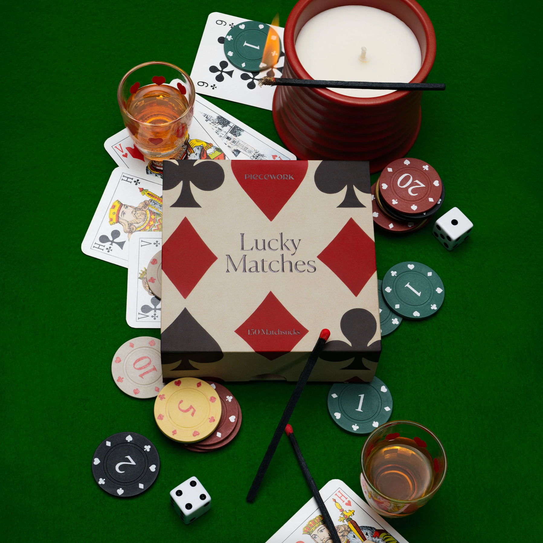 Candle, playing cards, poker chips, dice, and 'Lucky Matches' box on a green surface