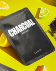 Black charcoal mask packaging with 'LAPCOS' branding on a yellow background with citrus fruits.