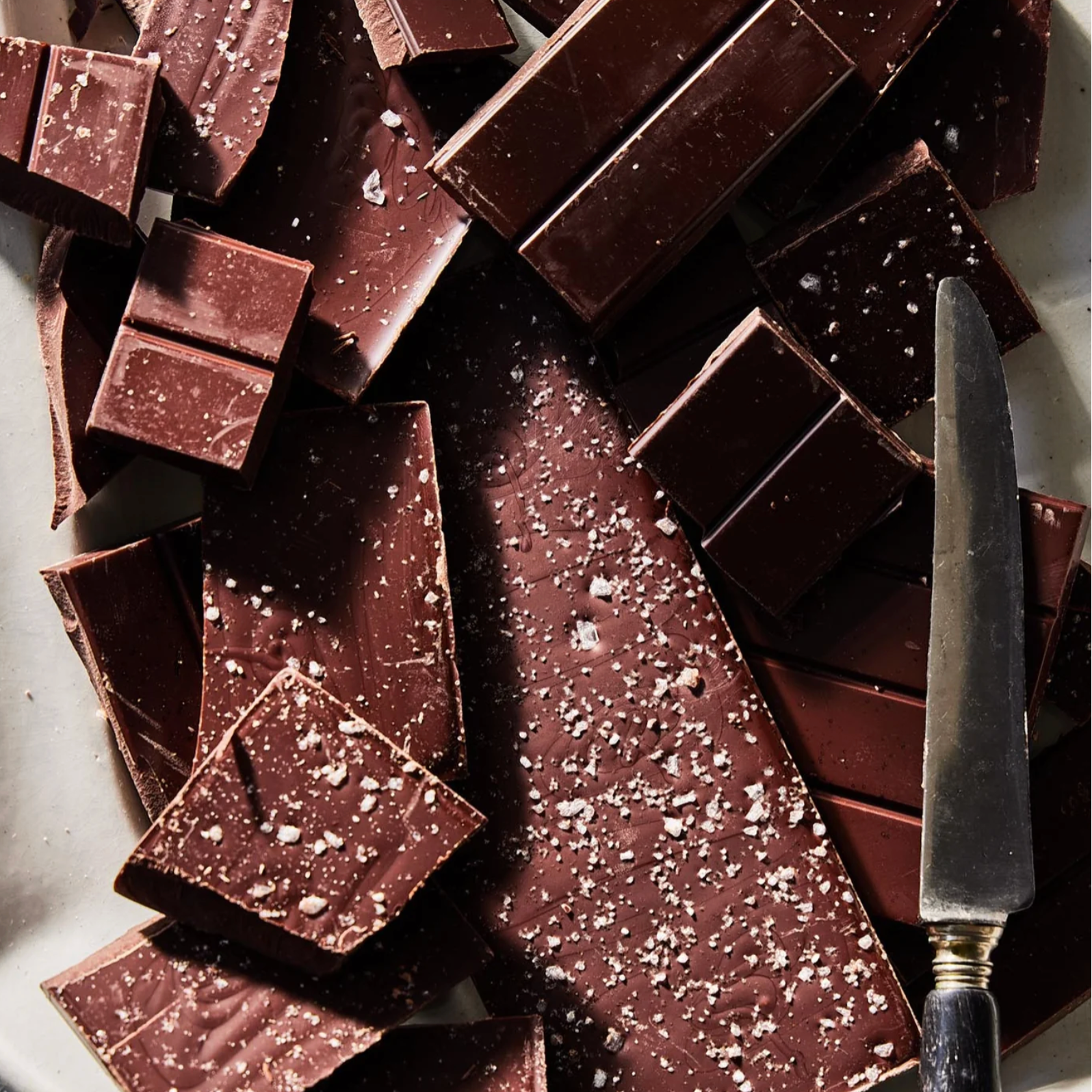 Dark chocolate bars with a knife on a white surface