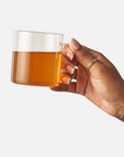 Hand holding a glass mug with amber liquid against a white background