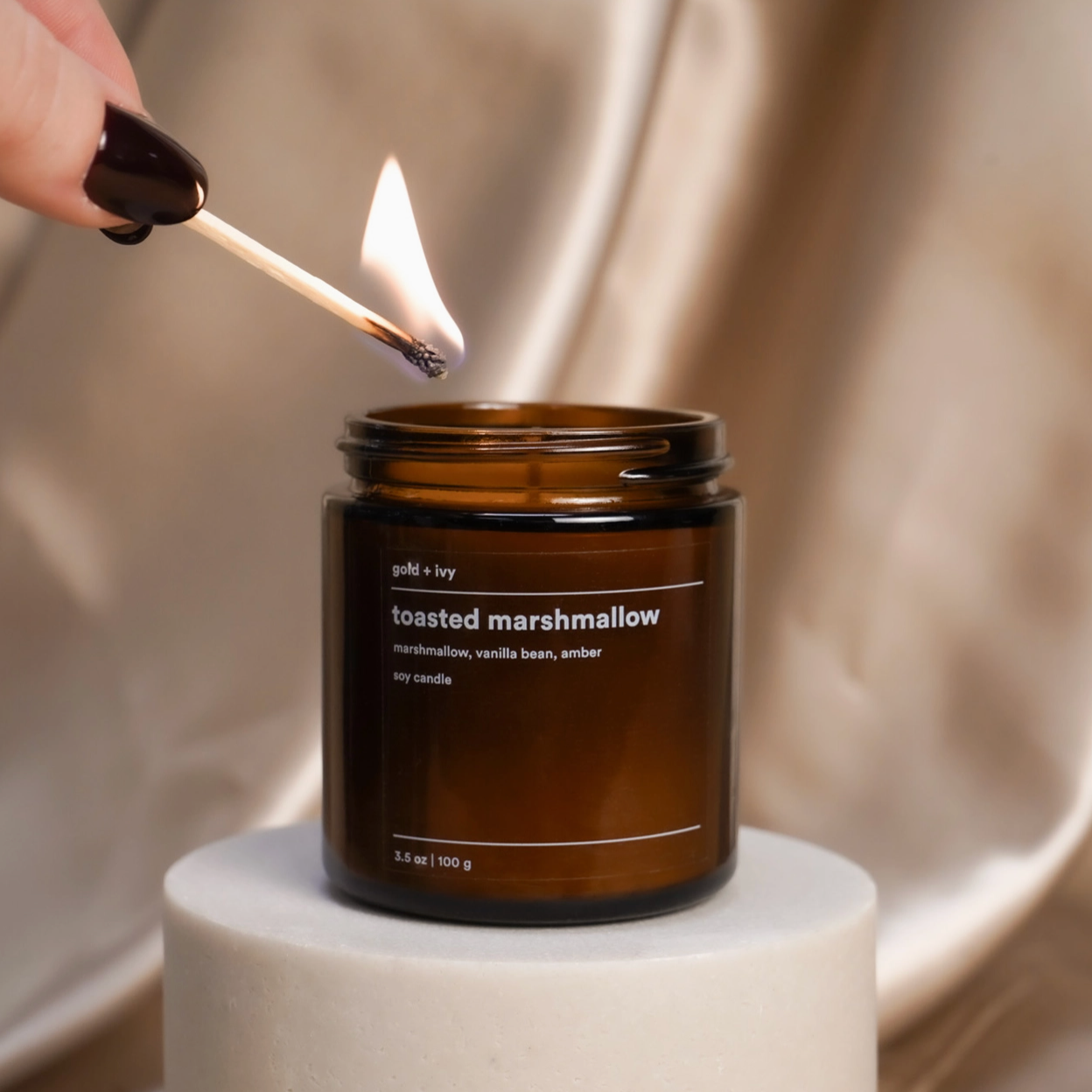 Person lighting a candle labeled 'toasted marshmallow' with a match.