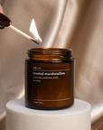 Person lighting a candle labeled 'toasted marshmallow' with a match.