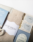 Gift set with mug, tea, socks, and bath items in a box on a white background