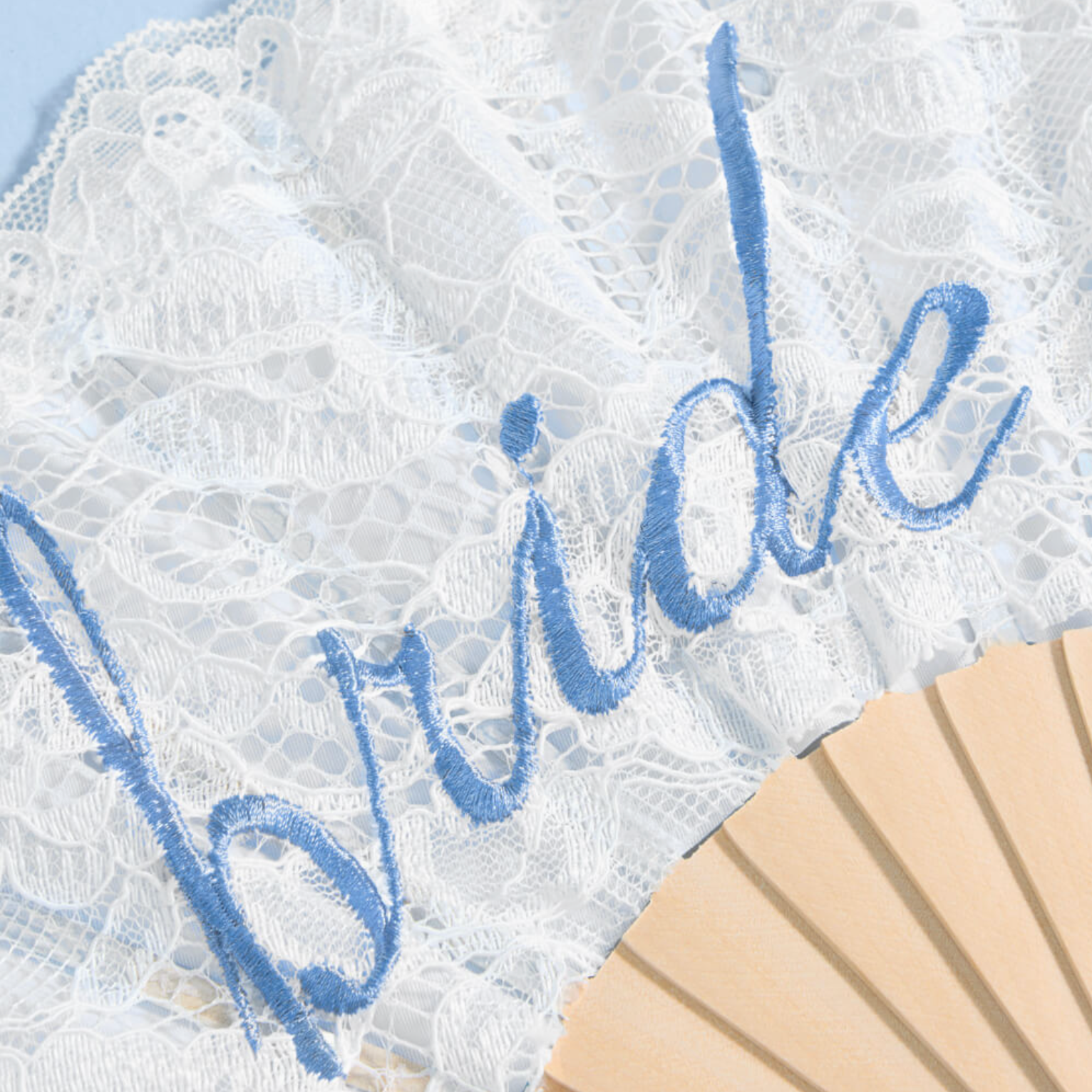 White lace fan with blue embroidered script reading 'Bride' and a light wood fan shaft visible at the bottom right.