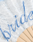 White lace fan with blue embroidered script reading 'Bride' and a light wood fan shaft visible at the bottom right.