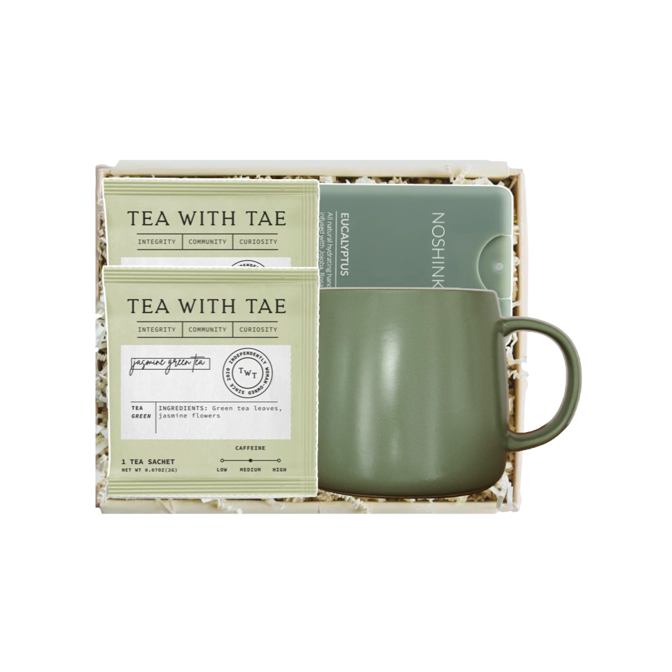 A tea gift set in a square box, featuring two packets of Tea With Tae matcha tea and a matte sage green ceramic mug with a matching lid, displayed on a white background.