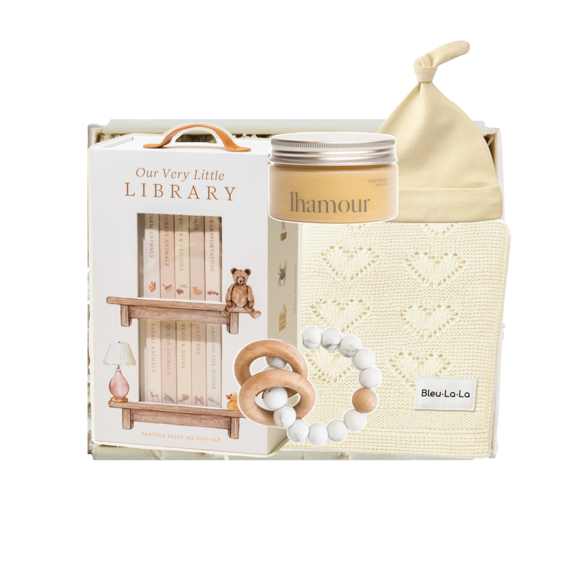 A baby gift set featuring a wooden toy library bookshelf, a cream-colored 'Ihamour' jar candle, a knitted cream baby blanket with heart patterns, and a wooden teething ring with white beads, all arranged in a white gift box.