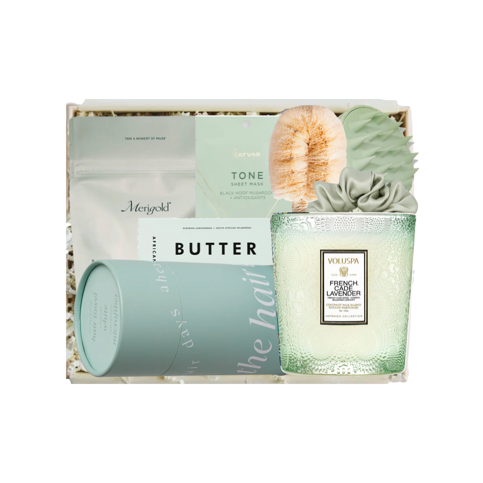 A curated gift box set containing a Holiland French Gardenia scented candle, a light blue cylindrical tin, a white pouch of Butter, a green soap bar, and a succulent, arranged in a box with gold crinkle paper.