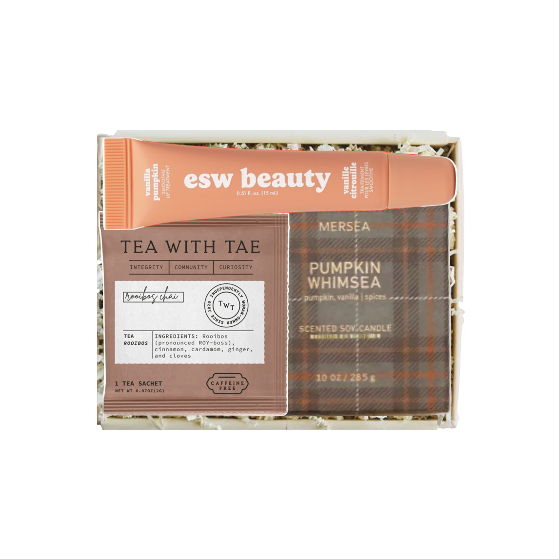 A boxed fragrance gift set from esw beauty, featuring a scented soap candle in a brown plaid tin labeled 'Pumpkin Whimsea', a brown paper card reading 'Tea with Tae', and an orange tube labeled 'esw beauty'. The set is presented in a clear box with shredded paper filler on a white background.