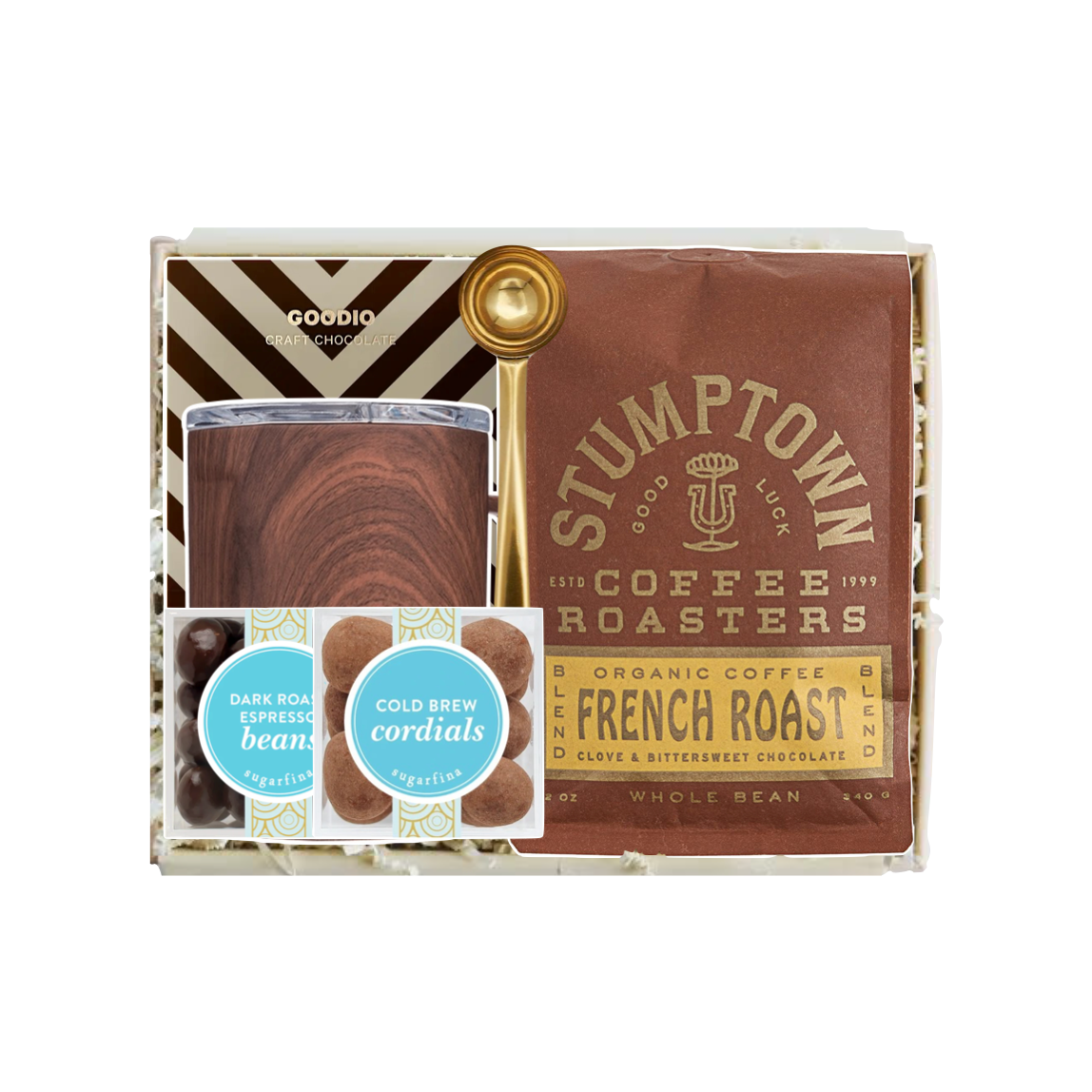 A coffee gift set in a clear window box package, featuring a brown Stumptown French Roast coffee bag, a glass carafe with dark roasted coffee, a gold spoon, and two small cold brew packets, arranged on white paper shred.