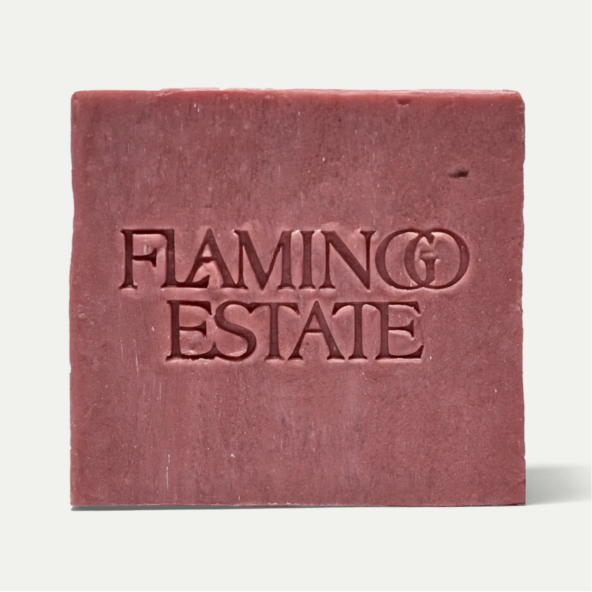 A square bar of dusty rose soap with the brand name 'FLAMINGO ESTATE' embossed on the front, set against a clean off-white background.