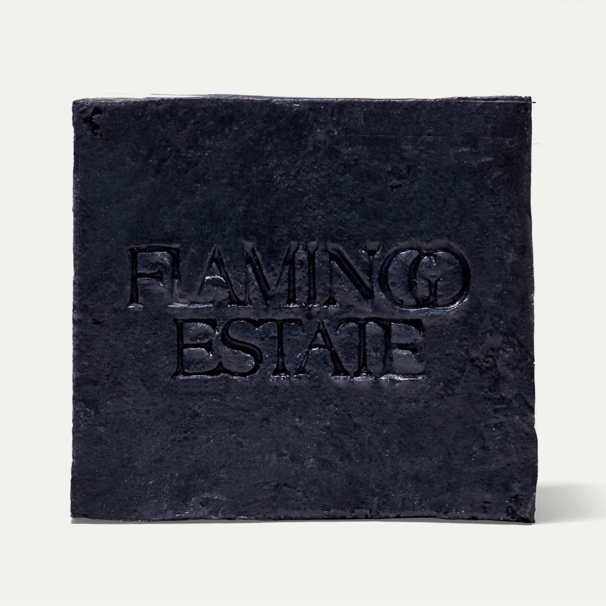 A square dark charcoal stone tile coaster embossed with the text 'FLAMINGO ESTATE' in a serif font, set against a clean off-white background.