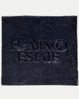A square dark charcoal stone tile coaster embossed with the text 'FLAMINGO ESTATE' in a serif font, set against a clean off-white background.