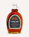 A bottle of Finding Home from Hudson Valley, New York maple syrup, filled with amber liquid, featuring a white cap and a decorative black, red, and white label, set against a solid off-white background.