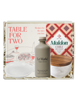 A gift set in a white box labeled 'TABLE FOR TWO' featuring a bottle of Le Marké Organic Olive Oil, a jar of Maldon Chili Sea Salt, and a printed recipe card, arranged with white filler.