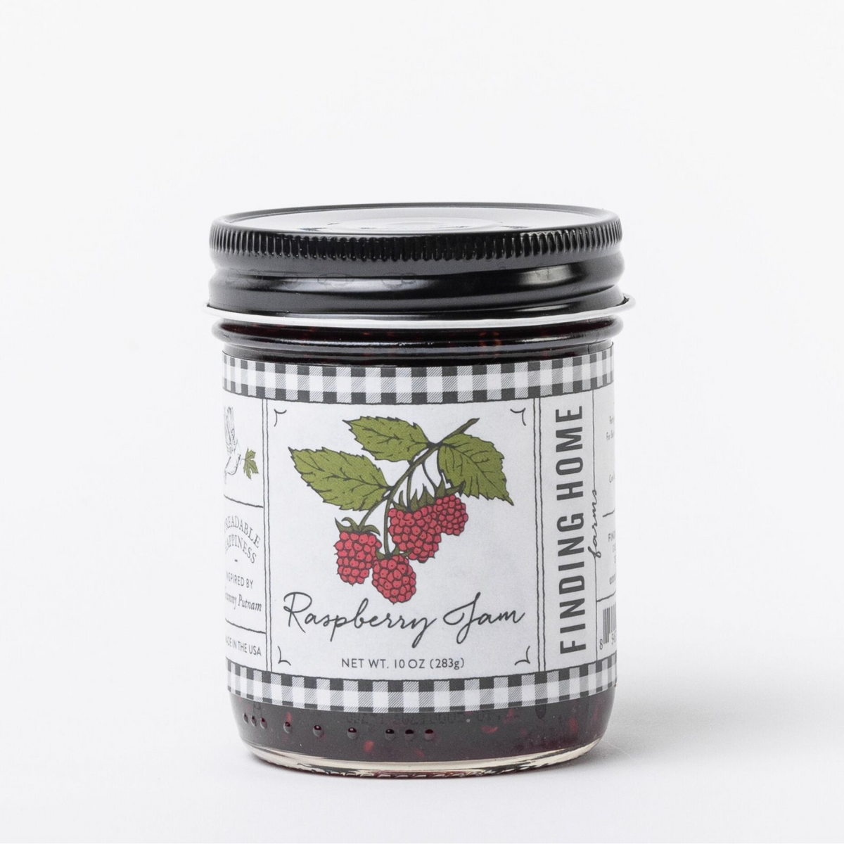 A glass jar of Finding Home Raspberry Jam with a black metal lid and a white label featuring a raspberry illustration, set against a plain white background.