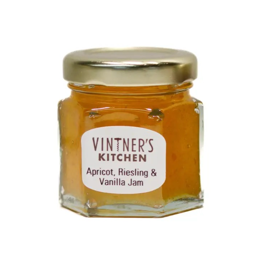 A small hexagonal glass jar of Vintner's Kitchen Apricot, Riesling & Vanilla Jam with a gold metal lid and a white label, set against a plain white background.