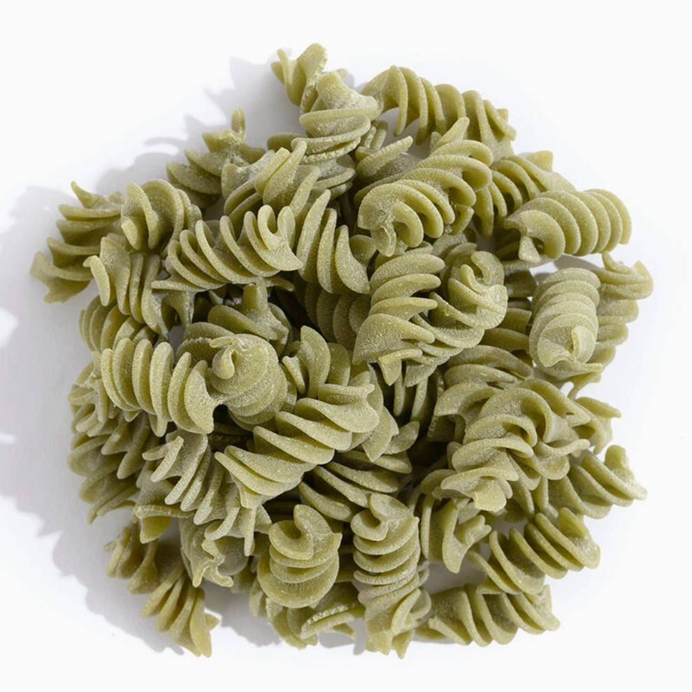 A pile of green rotini pasta on a clean white background with a soft shadow.