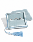 A light blue velvet ring box with a tassel, shown open with three silver rings inside on a white background.