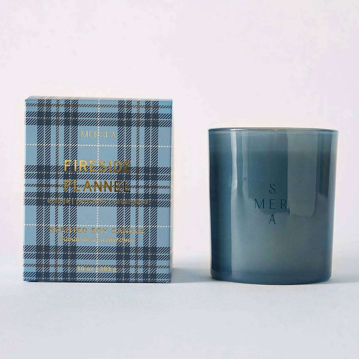 A candle jar in smoky translucent blue-gray glass stands beside its retail box. The box has a light blue plaid pattern with gold foil text reading 'FRENCH PLANNED' and 'CANDLE'.