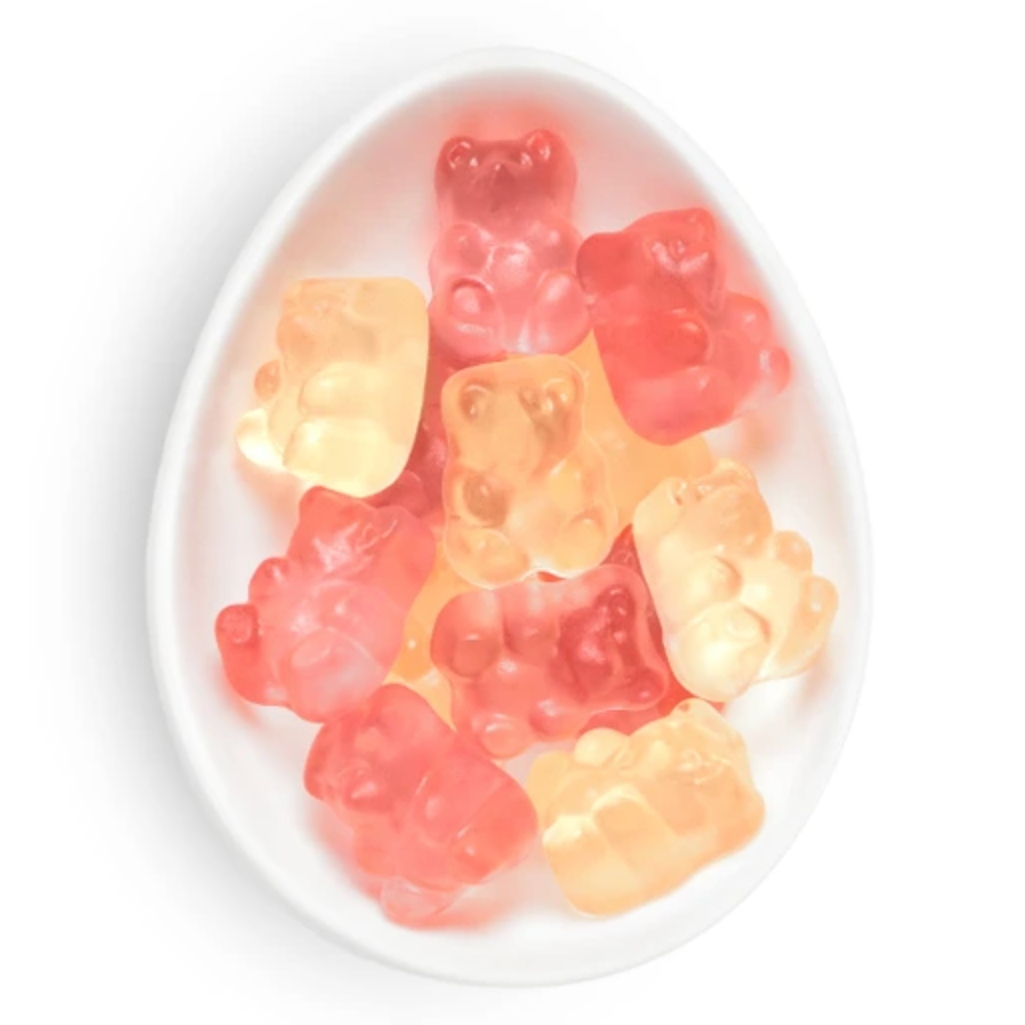 Gummy bear candies in assorted translucent colors, including pink, red, orange, and pale yellow, arranged inside a white oval dish on a white background.