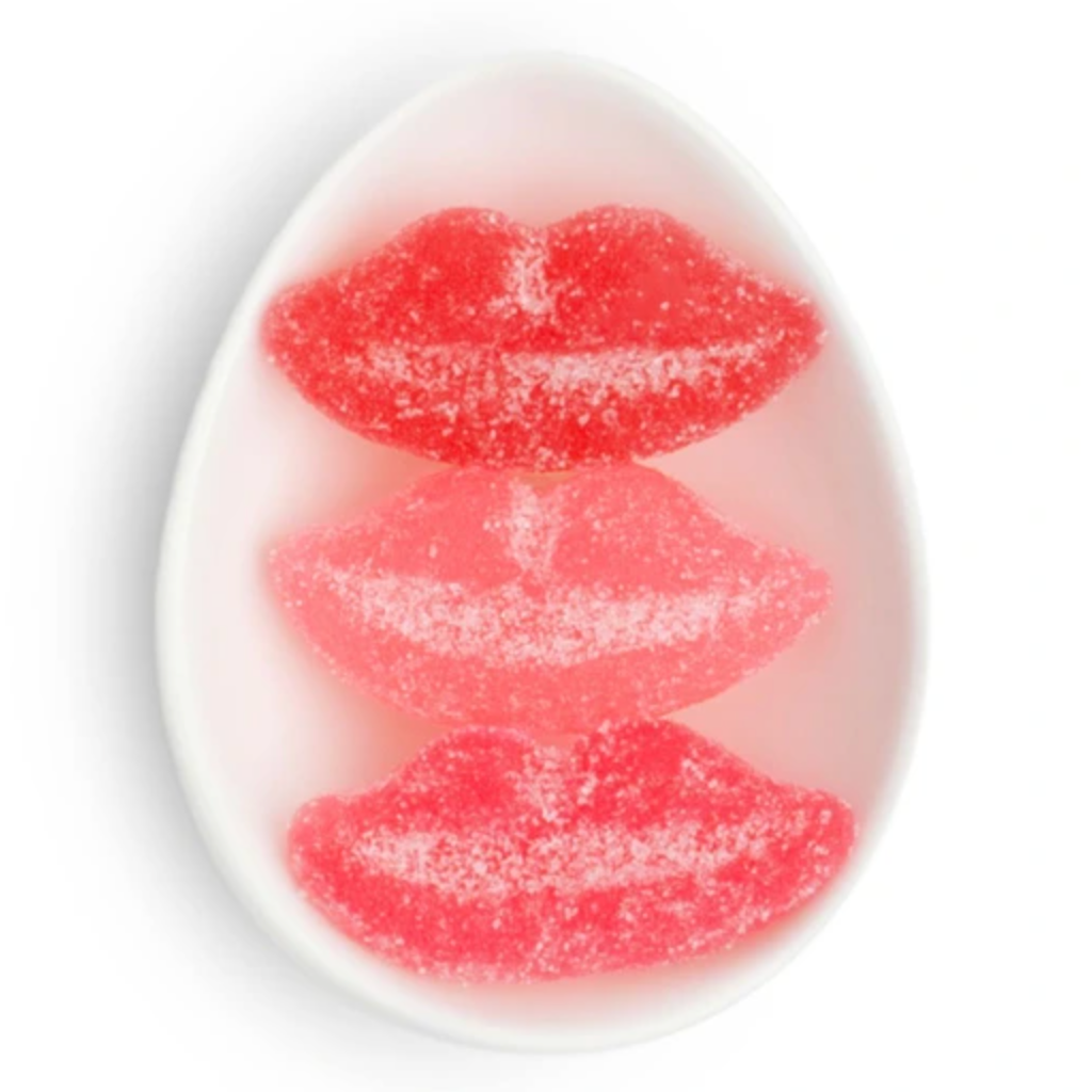 Three sugar-coated lip-shaped gummy candies stacked vertically in a white oval dish on a white background.