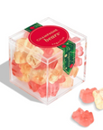 A clear cube-shaped container filled with colorful gummy bears, with a red round label reading 'CHAMOMILE BEARS' and a few gummy bears placed outside the container on a white background.