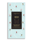 A sugarfina espresso martini dark chocolate bar in its packaging, featuring a light blue background with whimsical illustrations of skiers and a large black central label.