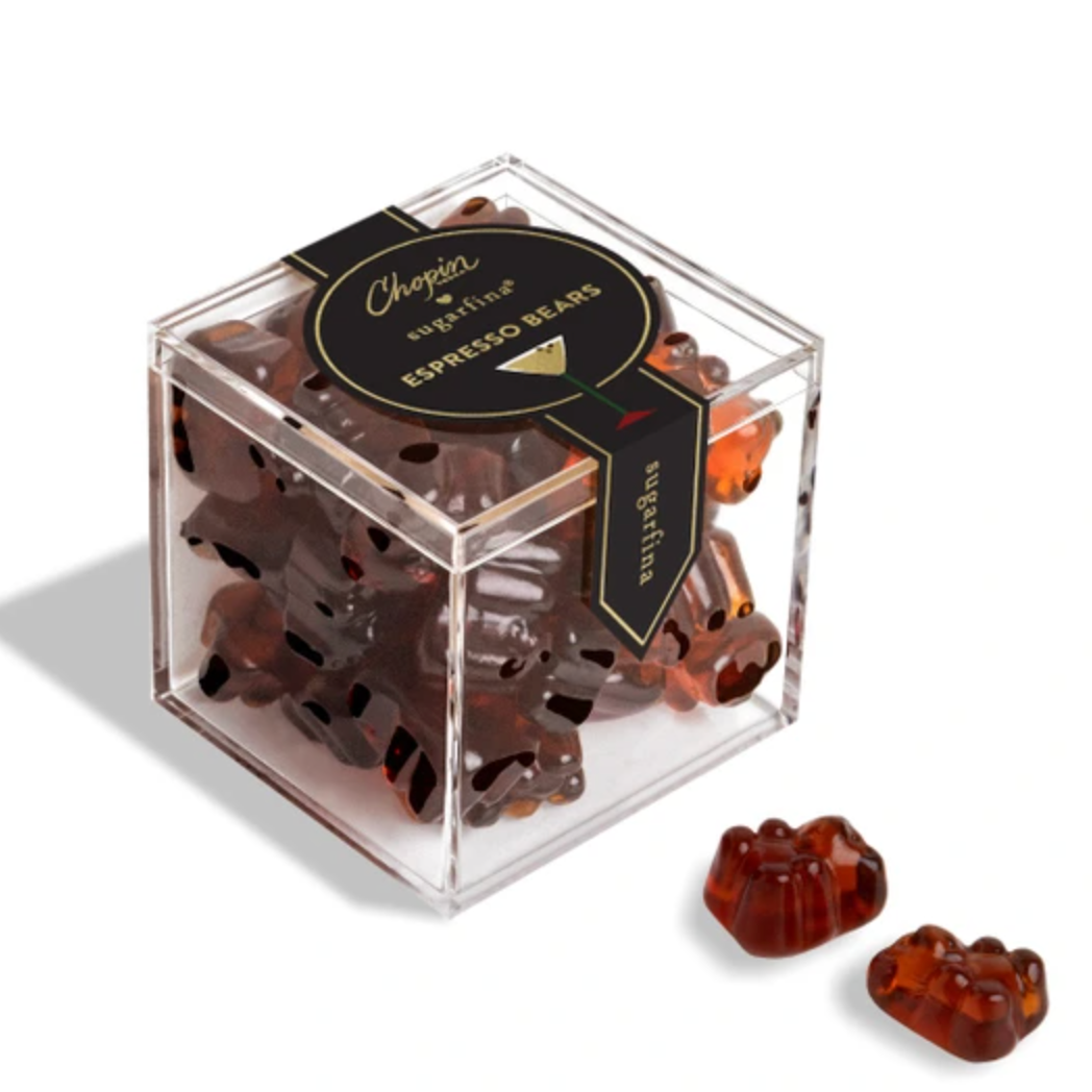 A clear acrylic cube container filled with espresso bean gummy bears, with two gummy bears placed outside the box on a clean white background. The box has a black lid and a black ribbon label with gold lettering that reads 'Chocolat Artisan Espresso Bean Gummies'.