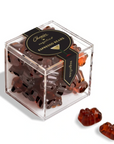 A clear acrylic cube container filled with espresso bean gummy bears, with two gummy bears placed outside the box on a clean white background. The box has a black lid and a black ribbon label with gold lettering that reads 'Chocolat Artisan Espresso Bean Gummies'.