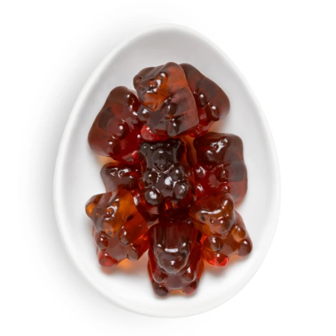 Glossy translucent red-brown gummy bears arranged in a white oval dish on a clean white background.