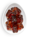 Glossy translucent red-brown gummy bears arranged in a white oval dish on a clean white background.