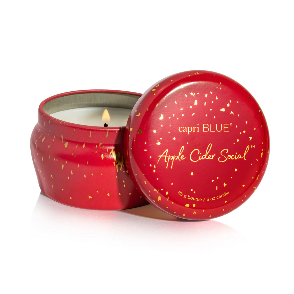 An open red metal candle tin with a matching lid leaning against it on a white background. The lid is printed with the brand name 'capri BLUE' and the scent name 'Apple Cider Social' in gold lettering.