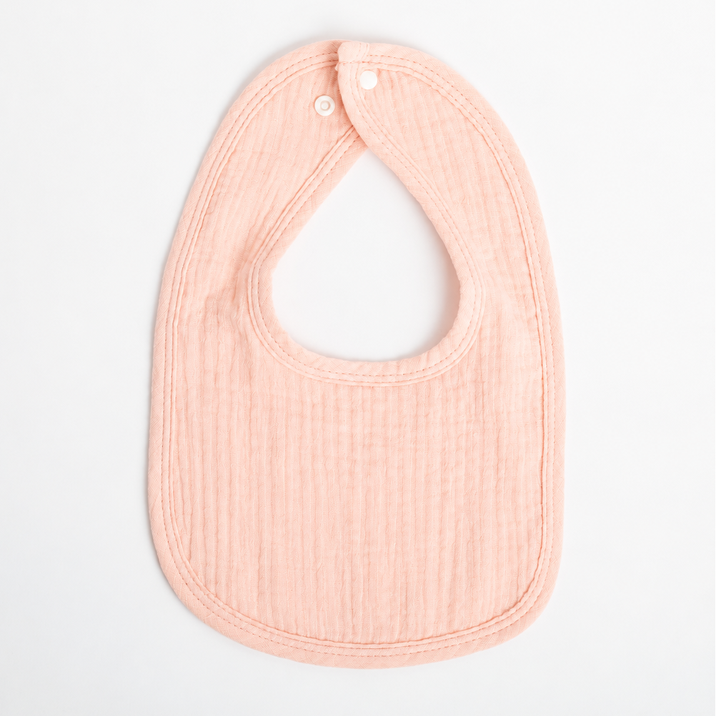 A pale peach muslin baby bib with the name 'Savannah' embroidered in white script across the front, displayed flat against a clean white background.