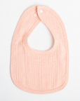 A pale peach muslin baby bib with the name 'Savannah' embroidered in white script across the front, displayed flat against a clean white background.