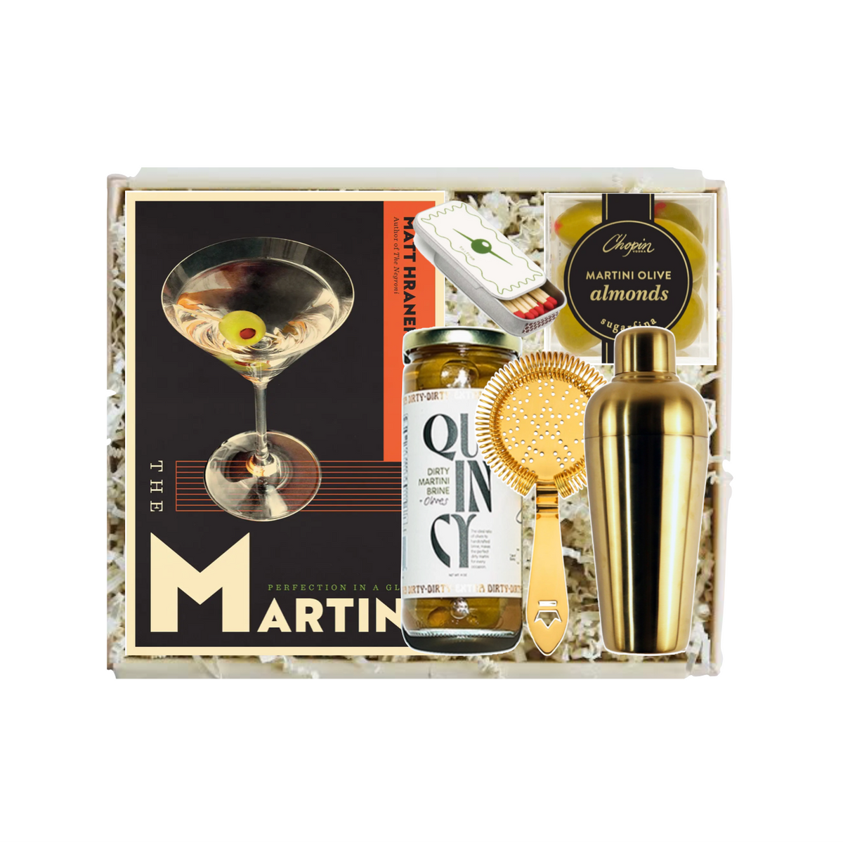A curated gift box set from The Martin Bar featuring a gold cocktail shaker, a bottle of Martin's Olives Almonds, a gold strainer, and a branded cocktail card, all arranged in white paper shred inside a gift box.