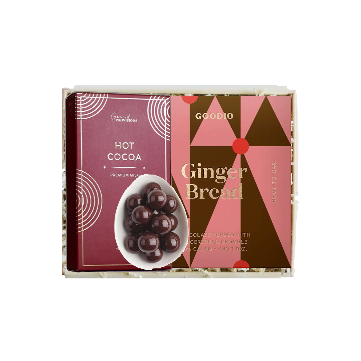 A boxed gift set from Goodoo Theorations featuring gingerbread cookies and hot cocoa. The packaging is a geometric pattern of pink, brown, and dark brown triangles with gold lettering, and a separate card on the left is labeled 'HOT COCOA' with an image of dark chocolate hot cocoa balls in a white bowl.