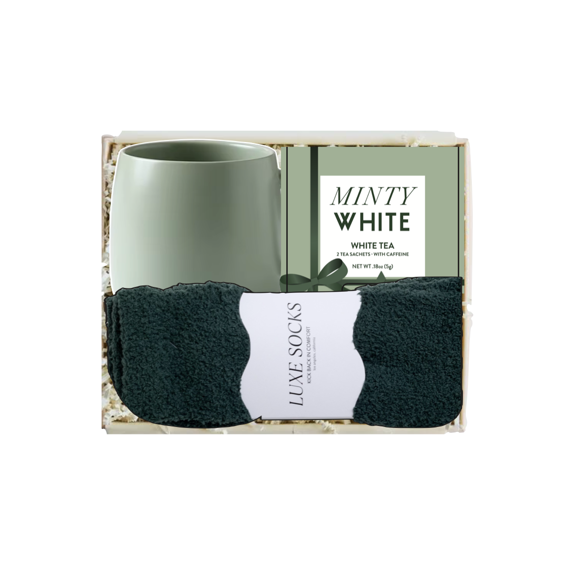 A gift set in a clear box containing a matte mint green ceramic mug, a pack of Luxe White tea bags, and a pair of dark charcoal gray socks with a white paper label.