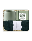 A gift set in a clear box containing a matte mint green ceramic mug, a pack of Luxe White tea bags, and a pair of dark charcoal gray socks with a white paper label.