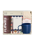 A curated gift box set containing a brown and white 'FLOWRS' notebook, a white notepad with a colorful border, a cream knit sock, and a blue ceramic mug, all arranged inside a light-colored box.