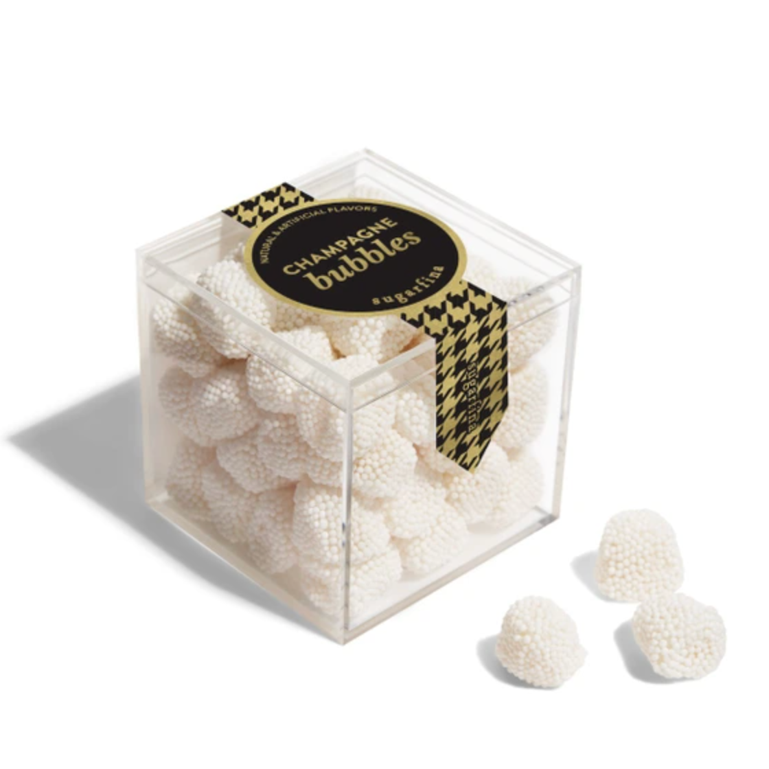 A clear acrylic cube container filled with small white textured gummy candies, tied with a black and gold houndstooth ribbon that reads 'CHAMPAGNE BUBBLES' and 'S. VILLE'.