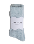 A pair of light blue fuzzy socks bundled together with a white paper label that reads 'LUXE SOCKS'.