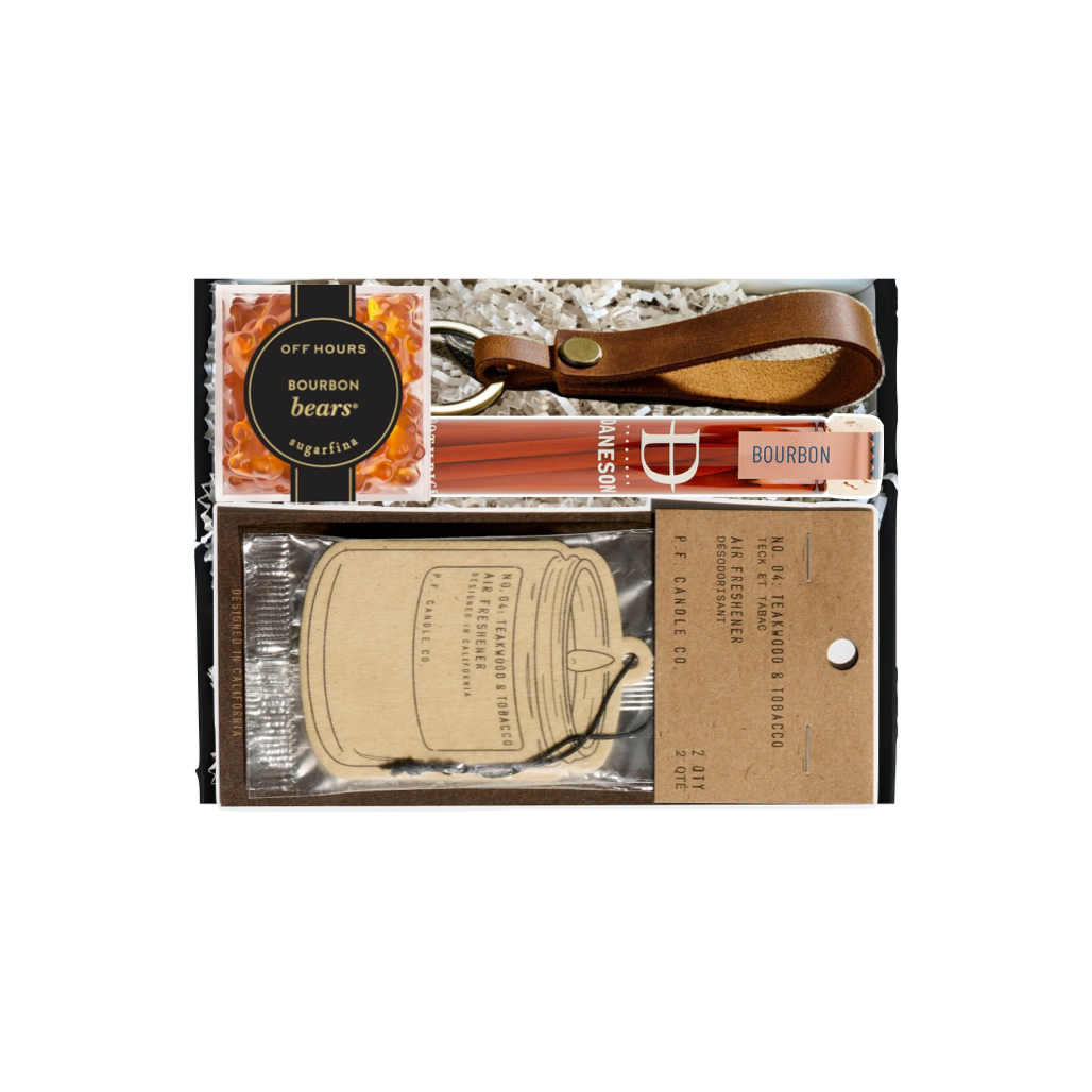 A boxed gift set containing a brown leather whiskey bottle strap, a bottle of bourbon barrels, a bag of Bourbon Barrel cookies, and printed labels inside a black gift box.