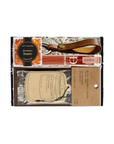A boxed gift set containing a brown leather whiskey bottle strap, a bottle of bourbon barrels, a bag of Bourbon Barrel cookies, and printed labels inside a black gift box.