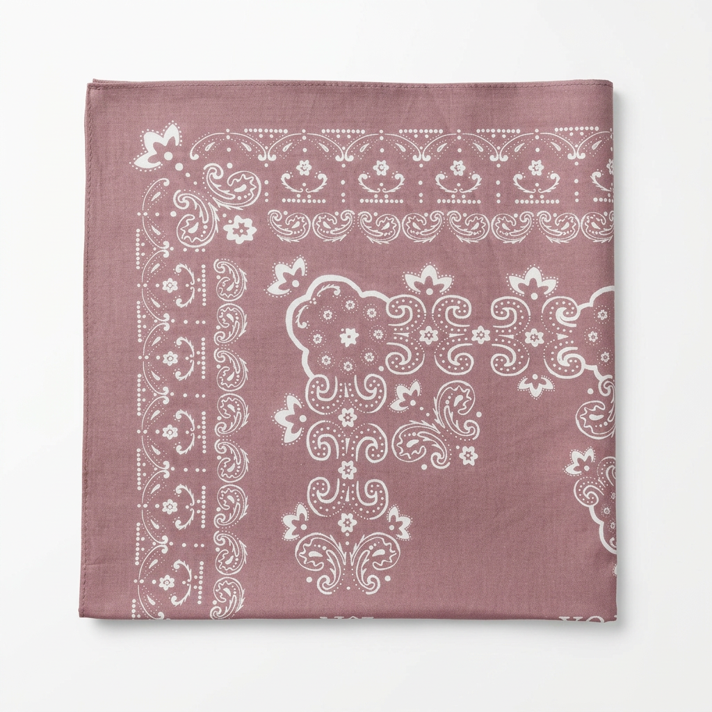 A square bandana or pocket square in dusty mauve with a white paisley and floral border pattern, laid flat on a light wood surface.