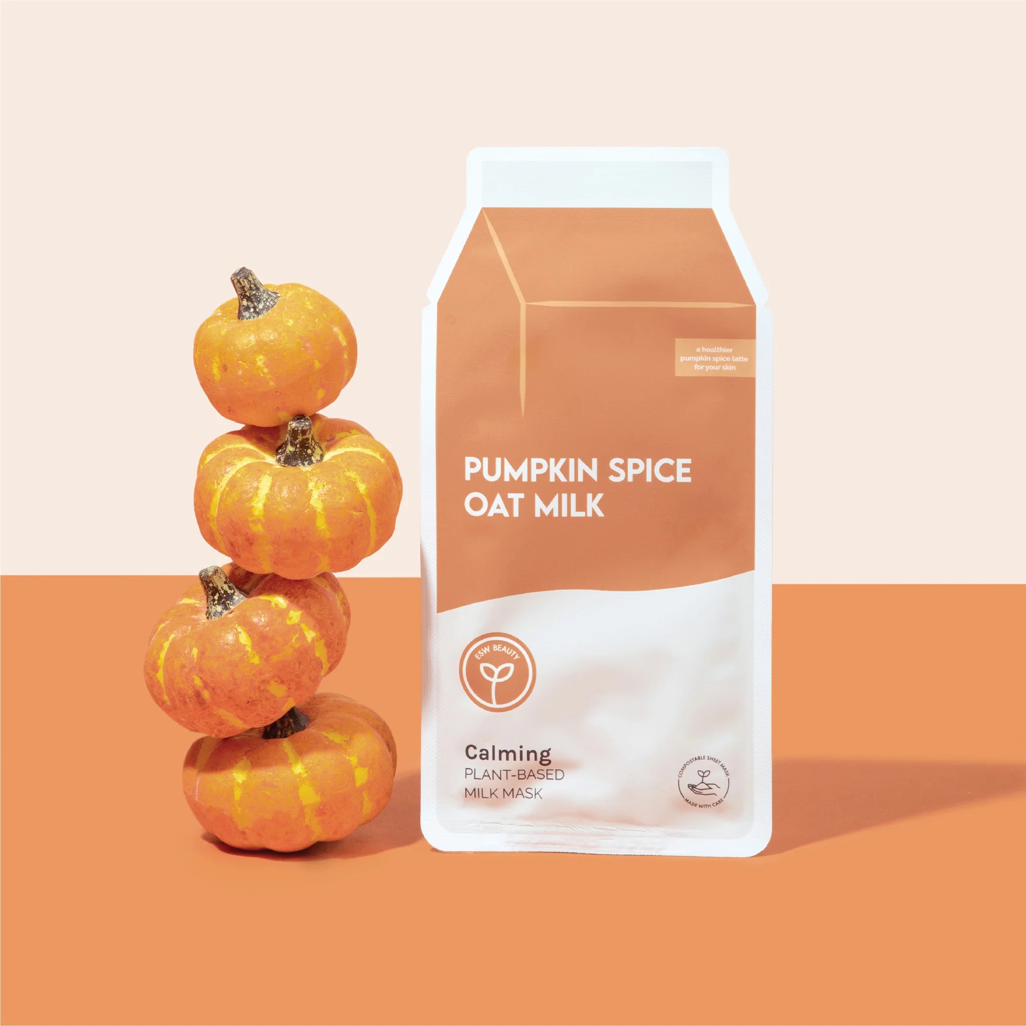 Pumpkin Spice Oat Milk Calming Plant-Based Milk Mask on orange and white background next to stack of mini pumpkins.