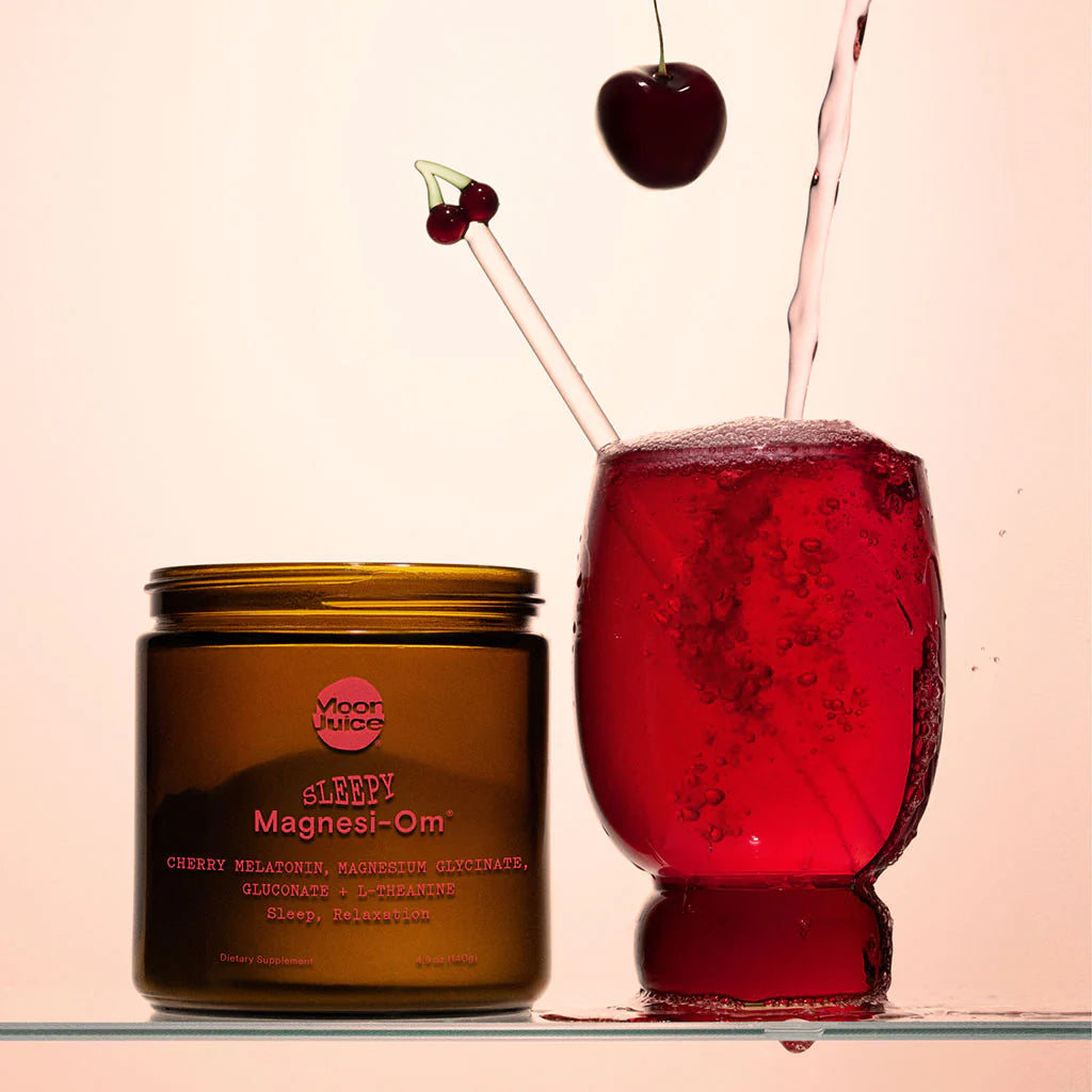Brown jar with pink writing that says "sleepy magnesi-om" and a clear glass with red liquid and a straw with a cherry on it and a cherry coming into the glass