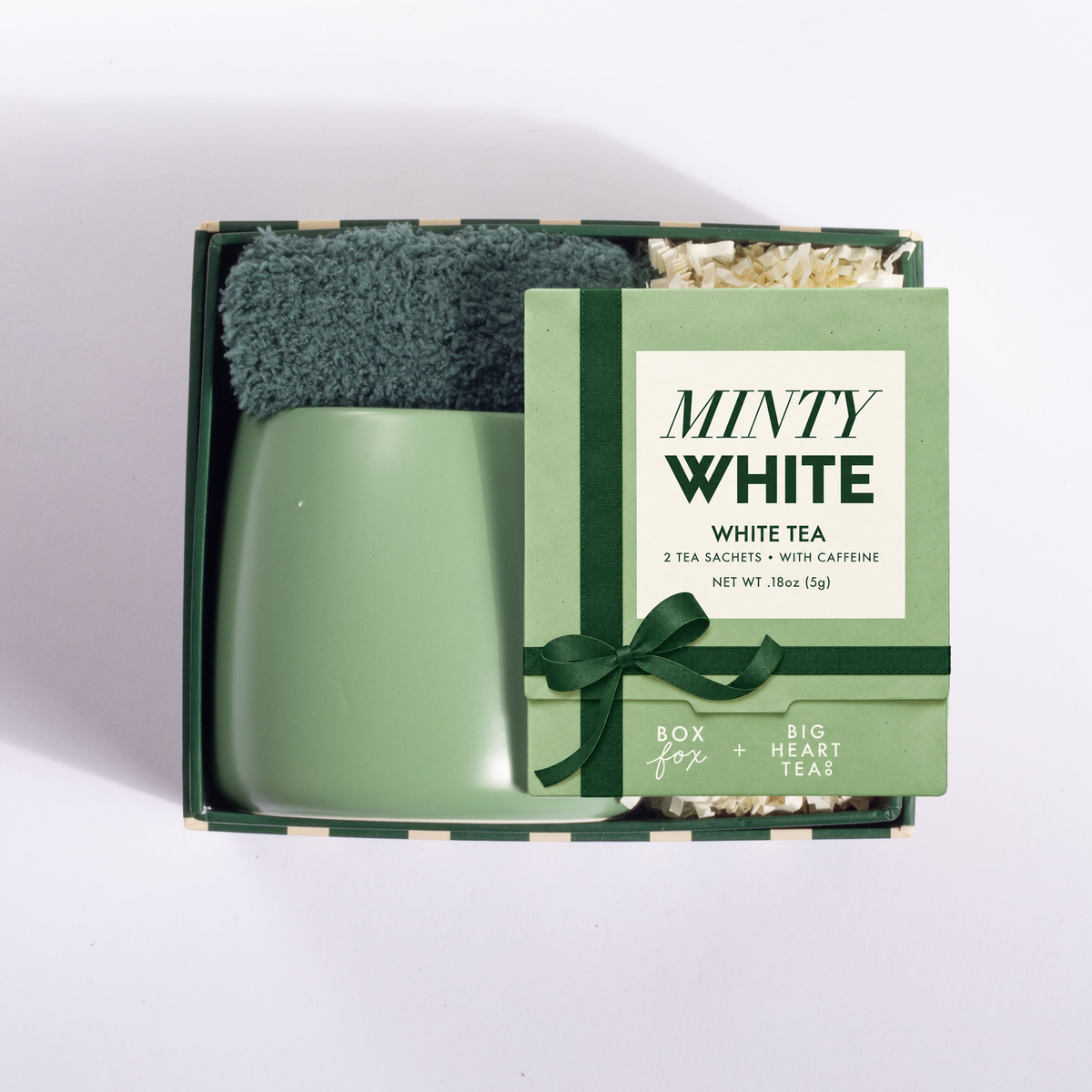 A mint green ceramic mug sits inside an open gift box with a matching green tea packet labeled 'MINTY WHITE' and a dark green scrubber, photographed on a clean white background.