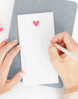 White notepad with neon pink hear on the top center